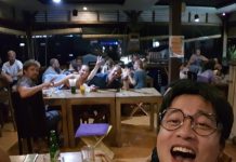 재미있고 기억에 남는 여행이란? 셀카를 찍는 뒷배경의 다른 테이블사람들이 카메라를 보고 v자 포즈를 취하며 환호중