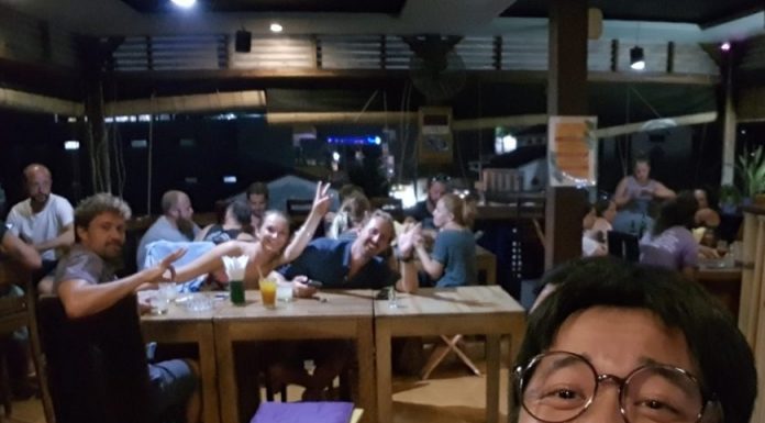 재미있고 기억에 남는 여행이란? 셀카를 찍는 뒷배경의 다른 테이블사람들이 카메라를 보고 v자 포즈를 취하며 환호중